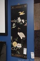 Front view of lacquered Asian style panel with birds and floral painted design hanging on a wall.