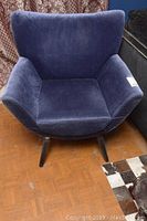 Front view of the blue velvet upholstered chair with angled wooden legs on parquet floor.