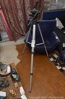 Full view of the Celestron tripod standing on a parquet floor with visible adjustable legs and head.