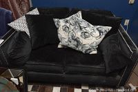 Full frontal view of black upholstered love seat with decorative pillows in various black and white patterns, showing nail head trim on arms.