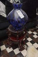 Blue glass vase sitting on top of two stacked Asian style wooden stands, showing overall appearance and condition including scratches.