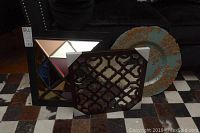 Two framed mirrors and a decorative plate shown from a distance on a rug in front of black furniture.