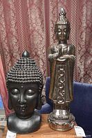 Two ceramic Buddha statues side by side against patterned curtain background, showing overall look and size relative to each other and tags at base.