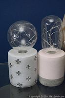 Photo showing two LED battery-powered lamps with different bases and glass covers containing LED lights.