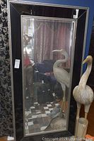 Full view of the large rectangular mirror with black frame and silver beaded trim, showing reflective surface and part of surrounding room.