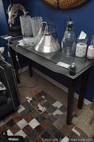 Full view of the hall table showing the glass top and black resin legs, surrounded by decorative items and furniture.