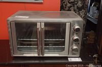 Front view of Oster convection toaster oven with glass door and dual handles on wire rack inside.