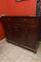 Front view of dark wood kitchen cabinet with two drawers and four doors on caster wheels