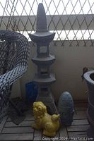 Full view of the yellow foo dog statue and the blue-gray Asian head sculpture placed on wooden slats, in front of a tall gray pagoda statue