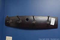 Full view of the dark wood coat rack mounted on blue wall showing its length, hooks, and mounting hole.