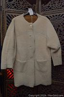 Full front view of beige shearling coat on hanger showing button closure and general shape