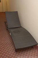 Full view of dark brown woven resin lounge chair with curved ergonomic design and metal frame.