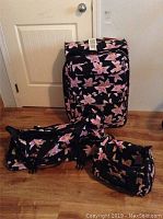 Three-piece floral luggage set including large suitcase, rolling tote, and small carry-on clustered together on a wood floor against a white door.