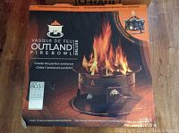 Photo showing front of the retail box of the Outland Firebowl Deluxe portable propane fireplace with flame image, control knob and product details.