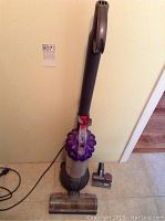 Full view of the Dyson DC 51 upright vacuum cleaner standing upright with power cord visible, two brush attachments on the floor next to it.