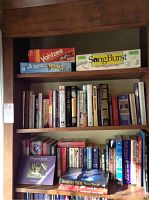 Shelf with a variety of books and three boxed board games on top: Yahtzee, Junior Scrabble, and Song Burst.