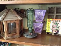 Wooden birdhouse, green glass hummingbird feeder, and two lavender grow kits on a shelf.