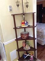 Corner shelf with four tiers holding Pooh and Eeyore plush, lamp base, doll tea set, and mobile visible beneath.