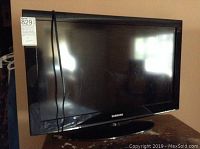 Front view of Samsung TV with power cable draped on screen and reflective surface showing surroundings.