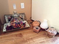 Photo of decorative mirrored shell-lined trays with large glass jar filled with purple and metallic baubles, salt lamps and aroma diffusers on side surface