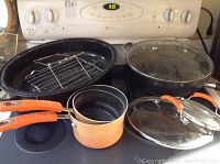 Overview of roasting pan, large pot with lid, and two saucepans with orange handles on stove.