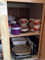 Cabinet shelf with ceramic soup bowls, plastic food containers, white ceramic bakeware and glass container with ceramic lid
