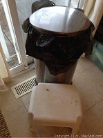 Full view of metal kitchen garbage can with black liner and white plastic step stool in front