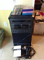 Full view of the karaoke machine showing cassette decks, equalizer controls, microphones, karaoke CDs, and user manuals.