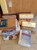 Assorted new linens stacked on the floor including duvet covers, pillow shams, sheet sets, and waterproof mattress cover in original packaging.