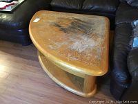 Wooden triangular lift top coffee table with worn, heavily marked top surface and visible scratches and discoloration. Lower shelf visible.