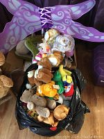 Photo showing a large black plastic bag filled with assorted TY stuffed animals including a tiger, bears, a frog, a penguin, and others.