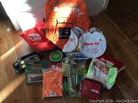 Orange Ready Kit plus backpack with St John Ambulance branding and various emergency kit items arranged around it on a wooden floor.