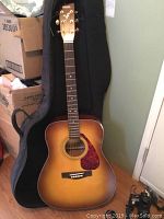 Full view of Yamaha F335 TBS acoustic guitar standing vertically inside its black soft carrying case in a room setting.