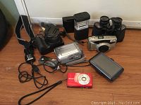 All items displayed on floor showing cameras, GPS device, accessories, and binoculars