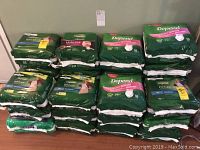 Large stack of green packages of Depend incontinence underwear for women with various sizes and counts visible, approximately 28 packages total.