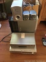 JVC surround sound system components including power subwoofer, satellite speakers, JVC DVD player and Electrohome VHS player stacked on top of each other with cables behind.