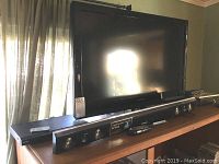 Dynex 37-inch LCD TV with Samsung Sound Bar in front of it, remote placed on the sound bar.