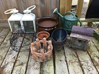 Photo showing the full collection of outdoor decor items including birdhouse, watering can, ceramic pots, wire hangers, and lanterns on a wooden deck.