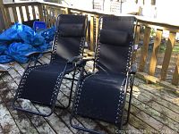 Photo displaying two black Mainstay gravity arm chairs set outside on a wooden deck with some outdoor debris nearby.