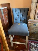 Photo of upholstered bar chair showing full front view with tufted back and wooden legs.