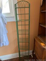 Tall green metal display shelving with wire shelves and arched top, against wall with window
