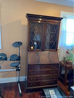 Front view of vintage wooden secretary desk with glass doors and drawers, showing details of wood grain, diamond muntin glass doors, and lower drawers.