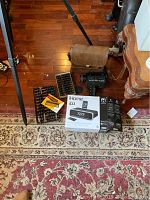 The entire lot laid out on a carpet showing the Bolex camera bag, iHome 433 boxed music player and alarm, two Abacuses with instruction booklets, and an iPhone charger box.