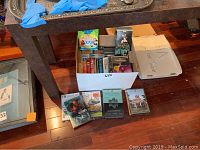 Box containing multiple DVDs and VHS tapes along with some DVDs laid out in front, including several movies and TV series cases.