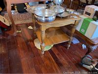 Wooden end table with lower shelf, visible scratches and crack, showing worn condition on hardwood floor.