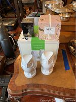 Lot displayed on wood table includes sealed black Lanvin Arpège perfume box and pink Nest Fragrances candle box behind a pair of white owl bookends with original box.