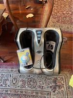 Photo of silver and black Comfy legs and feet massager with black fabric foot compartments and control panel showing blue buttons. Includes instruction manual and sealed Homedics SoundSpa Mini packaging beside it.