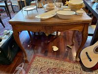 Front view of vintage expandable wooden buffet table with carved legs and detailed apron, showing surface marks and scratches.