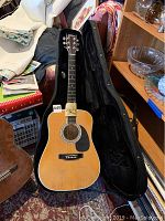 American Legacy acoustic electric guitar in original black hard case shown open, including guitar and some accessories around.
