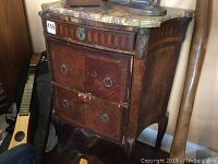Front and side view showing the three wooden drawers, carved wood details, metal drawer pulls, and the marble top with cracks and chips.